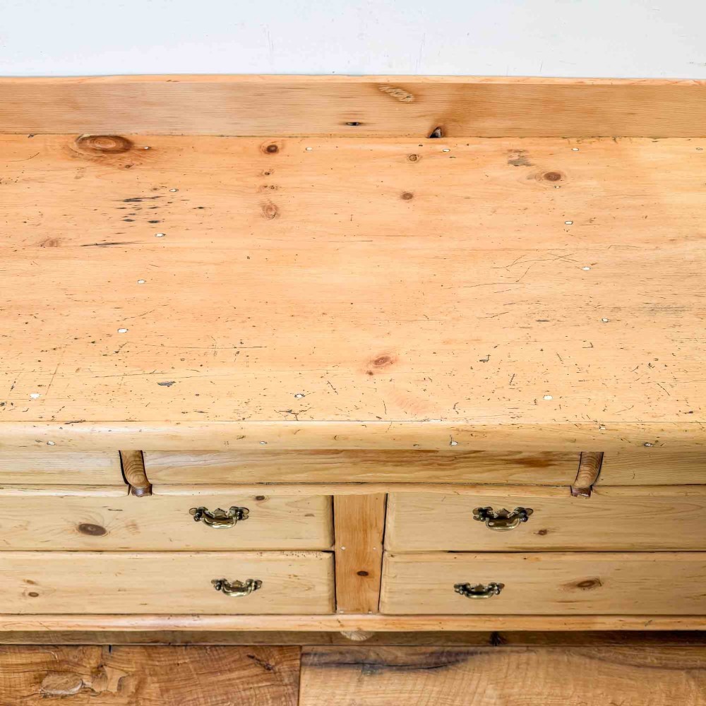 A Victorian natural pine dresser base featuring a low upstand back, seven drawers with metal drop handles, and turned bun feet. View XII