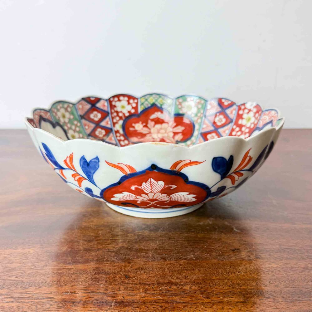 A shallow Japanese Imari porcelain bowl featuring a scalloped rim, hand-painted floral panels in cobalt blue, iron-red enamel, and green accents on a white porcelain ground.
