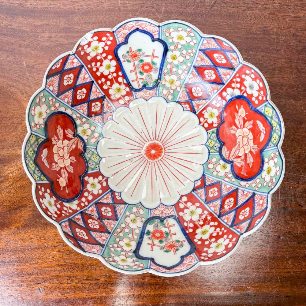 A shallow Japanese Imari porcelain bowl featuring a scalloped rim, hand-painted floral panels in cobalt blue, iron-red enamel, and green accents on a white porcelain ground. View III