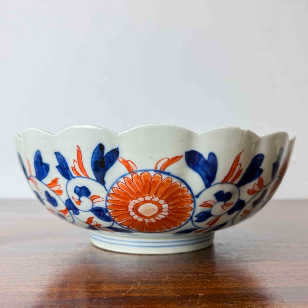 A shallow Japanese Imari porcelain bowl featuring a scalloped rim, hand-painted floral panels in cobalt blue, iron-red enamel, and green accents on a white porcelain ground. View IV