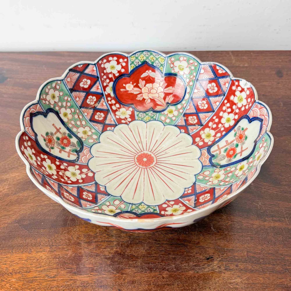 A shallow Japanese Imari porcelain bowl featuring a scalloped rim, hand-painted floral panels in cobalt blue, iron-red enamel, and green accents on a white porcelain ground. View V