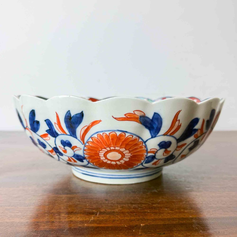 A shallow Japanese Imari porcelain bowl featuring a scalloped rim, hand-painted floral panels in cobalt blue, iron-red enamel, and green accents on a white porcelain ground. View VII