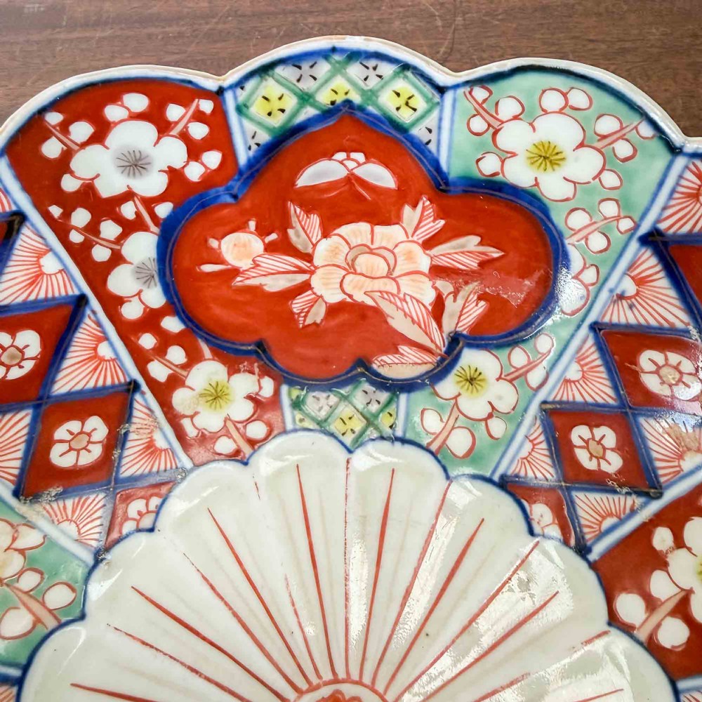A shallow Japanese Imari porcelain bowl featuring a scalloped rim, hand-painted floral panels in cobalt blue, iron-red enamel, and green accents on a white porcelain ground. View X