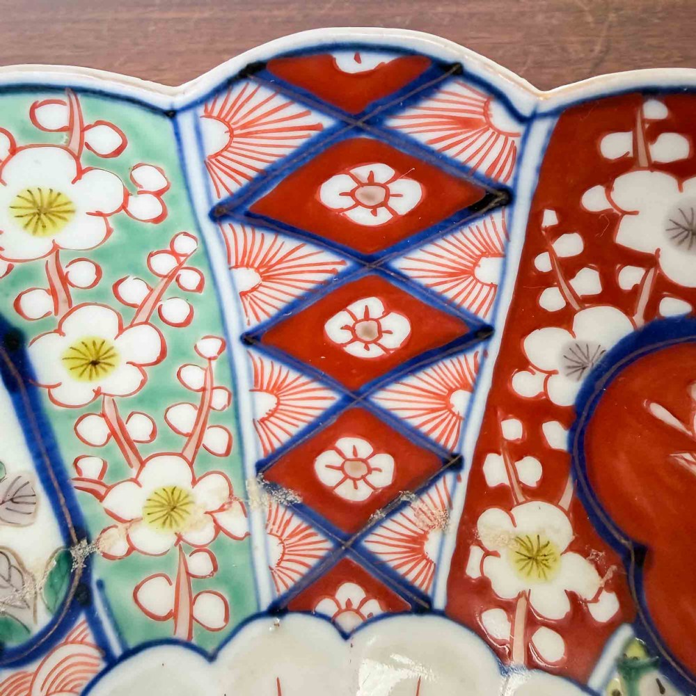 A shallow Japanese Imari porcelain bowl featuring a scalloped rim, hand-painted floral panels in cobalt blue, iron-red enamel, and green accents on a white porcelain ground. View XIII