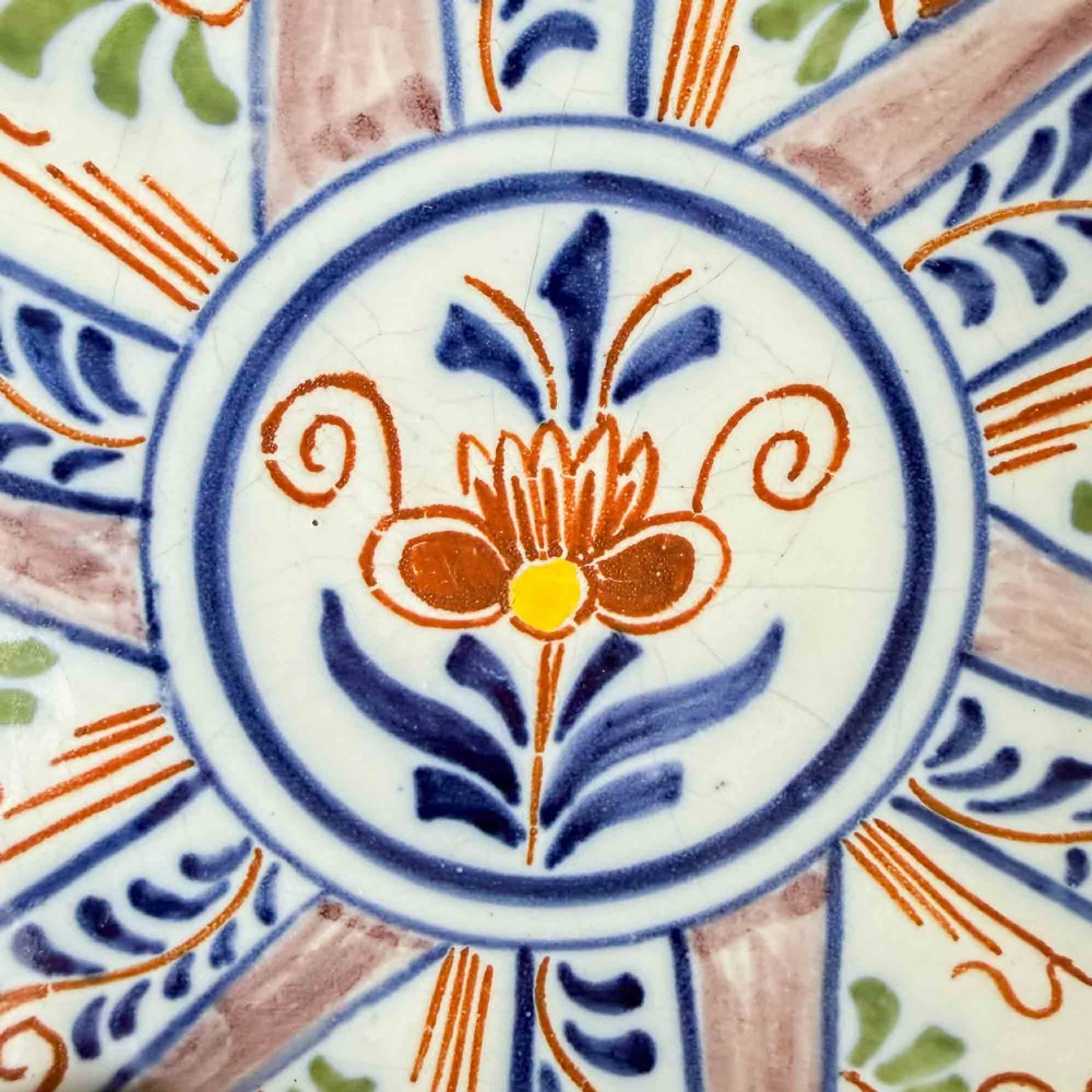 An antique circular tin-glazed earthenware plate decorated with hand-painted floral and geometric motifs in orange, cobalt blue, and brown over a pale green background. View V