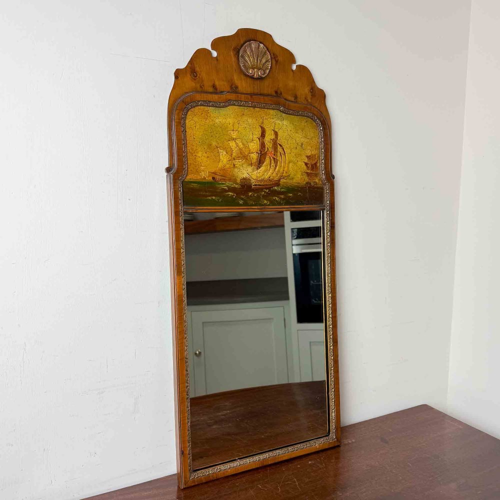 A tall Queen Anne Revival yew wood wall mirror featuring a carved shell crest at the top, an upper panel painted with a sailing ship maritime scene, and a rectangular glass mirror below.