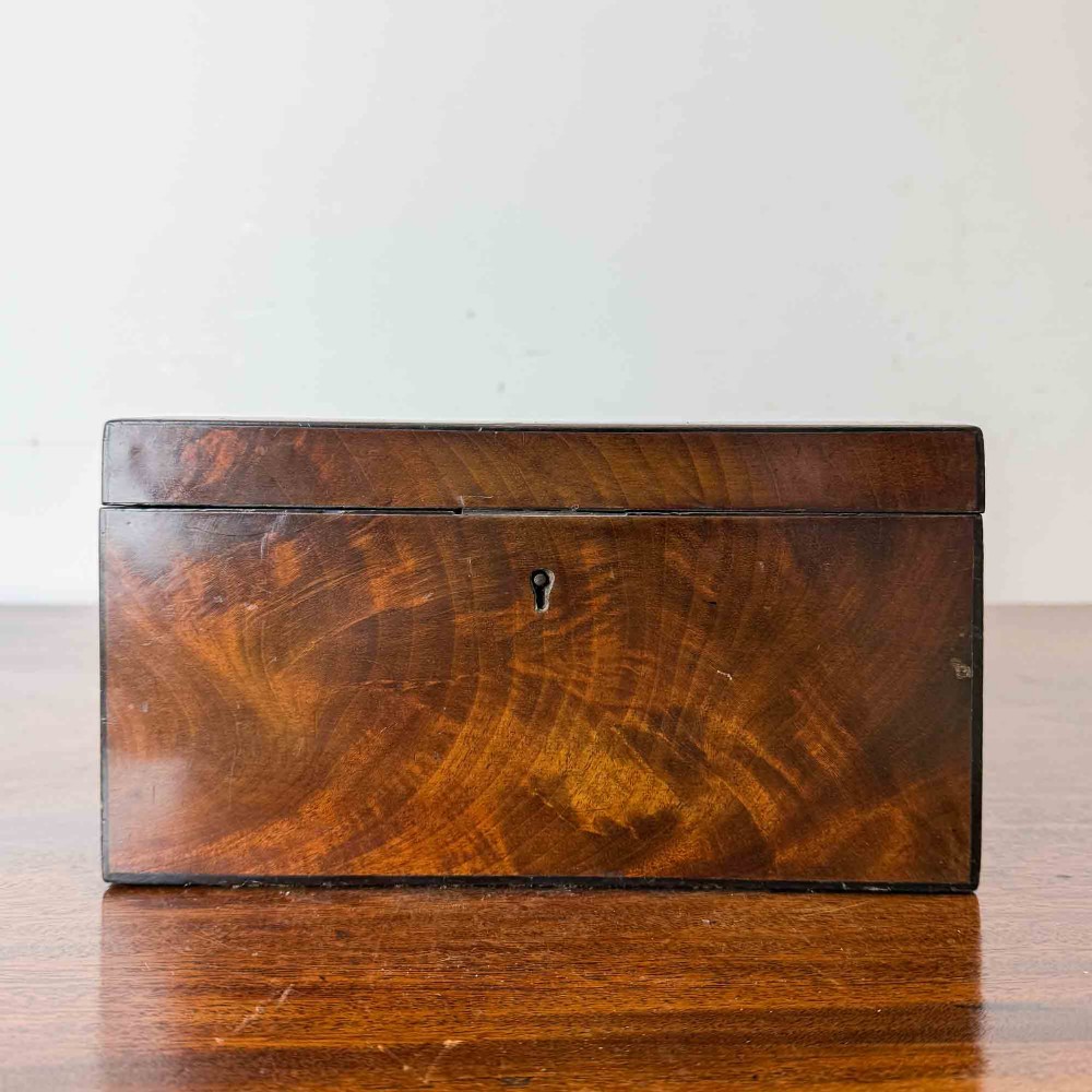 A rectangular early Victorian tea caddy crafted from flame mahogany veneer with crossbanded inlaid borders and a central metal keyhole escutcheon. View II