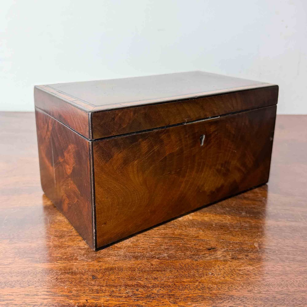 A rectangular early Victorian tea caddy crafted from flame mahogany veneer with crossbanded inlaid borders and a central metal keyhole escutcheon. View VI