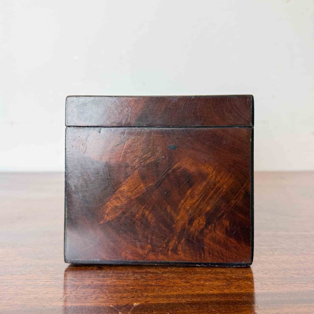 A rectangular early Victorian tea caddy crafted from flame mahogany veneer with crossbanded inlaid borders and a central metal keyhole escutcheon. View VII
