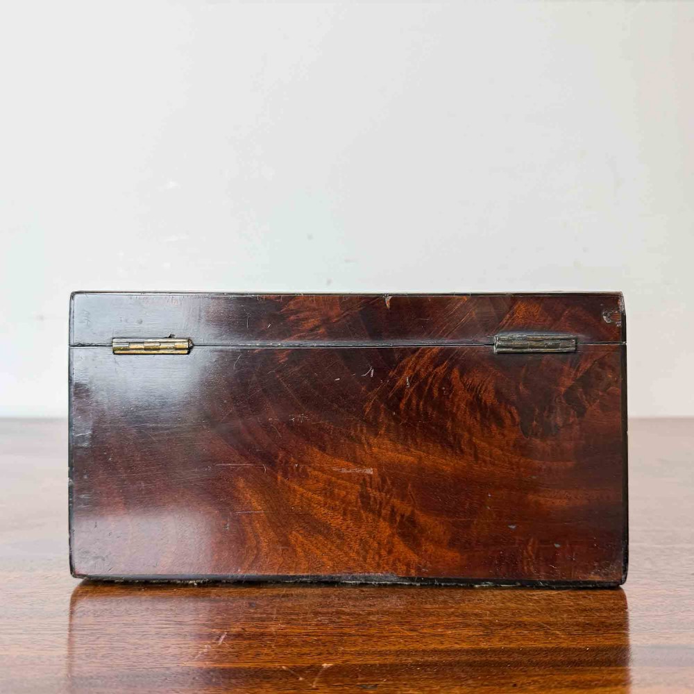 A rectangular early Victorian tea caddy crafted from flame mahogany veneer with crossbanded inlaid borders and a central metal keyhole escutcheon. View VIII