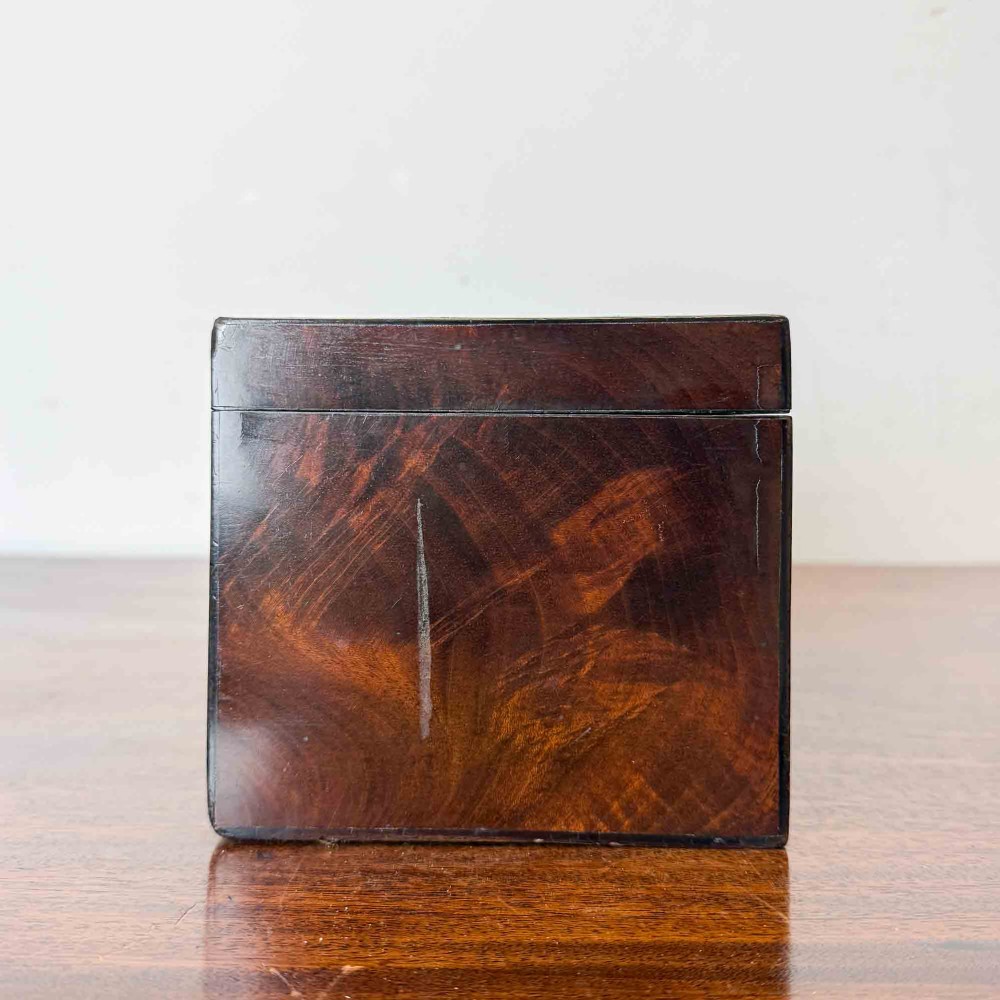 A rectangular early Victorian tea caddy crafted from flame mahogany veneer with crossbanded inlaid borders and a central metal keyhole escutcheon. View IX