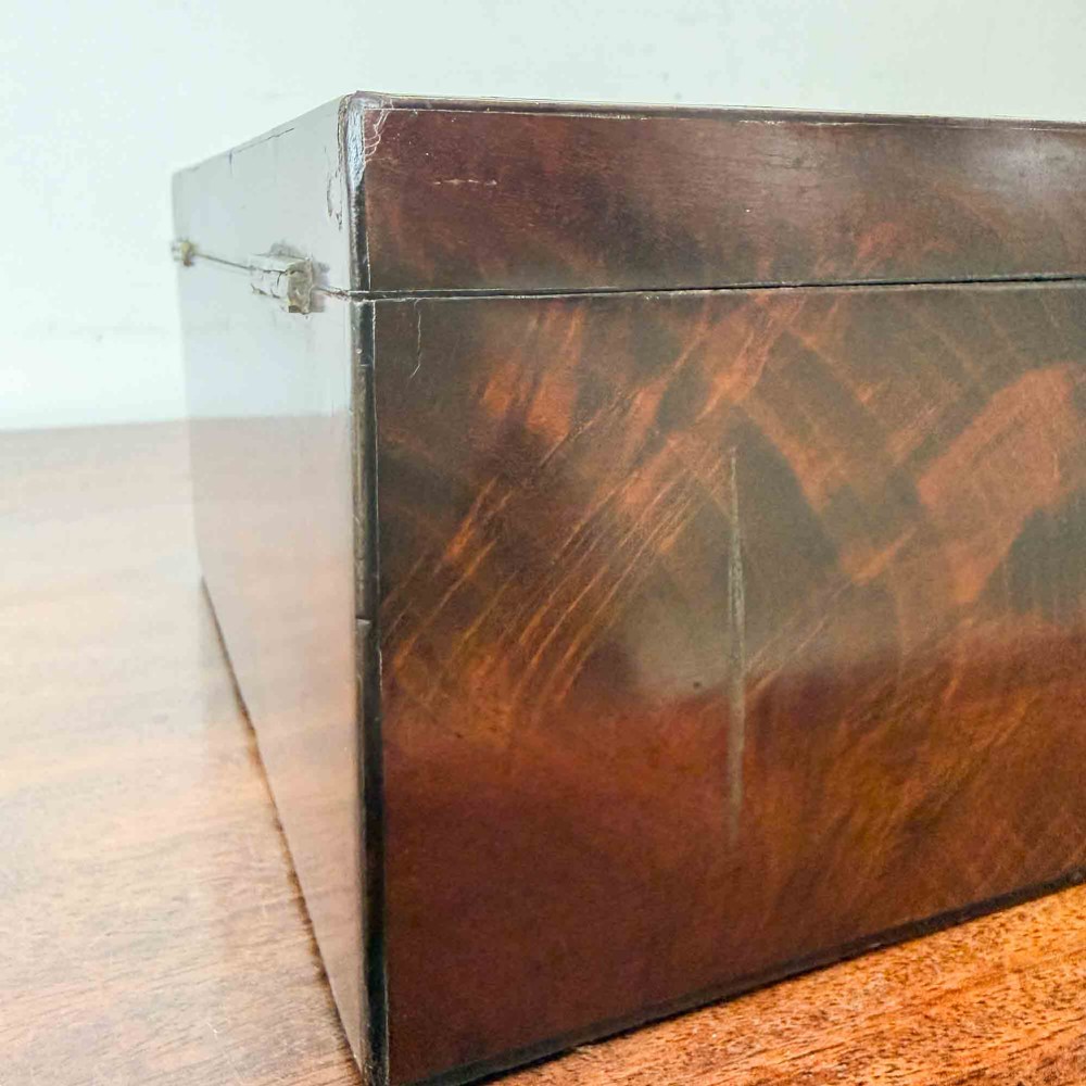 A rectangular early Victorian tea caddy crafted from flame mahogany veneer with crossbanded inlaid borders and a central metal keyhole escutcheon. View X