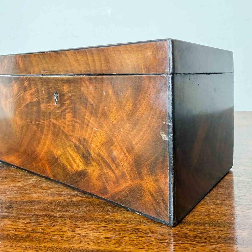 A rectangular early Victorian tea caddy crafted from flame mahogany veneer with crossbanded inlaid borders and a central metal keyhole escutcheon. View XI