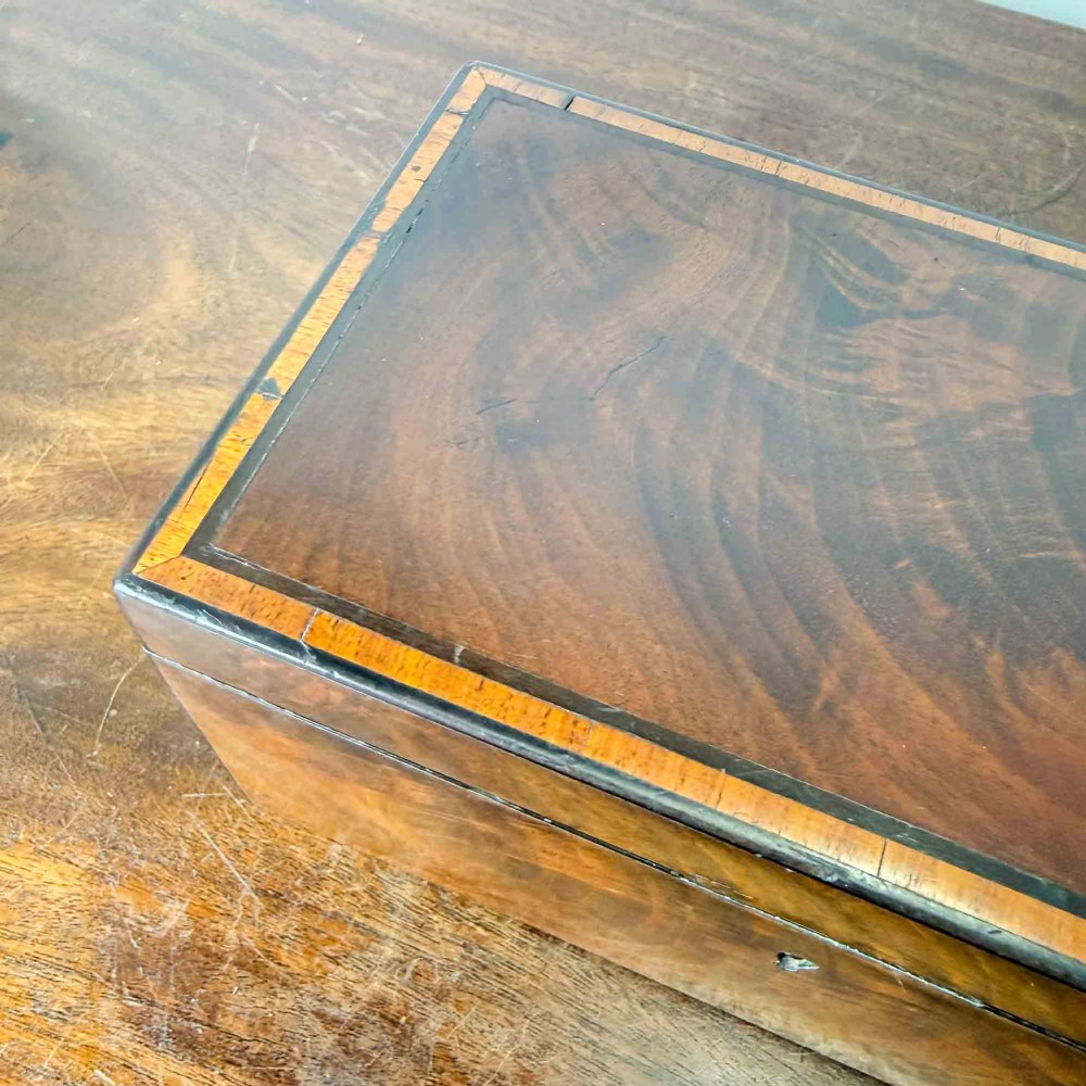 A rectangular early Victorian tea caddy crafted from flame mahogany veneer with crossbanded inlaid borders and a central metal keyhole escutcheon. View XII