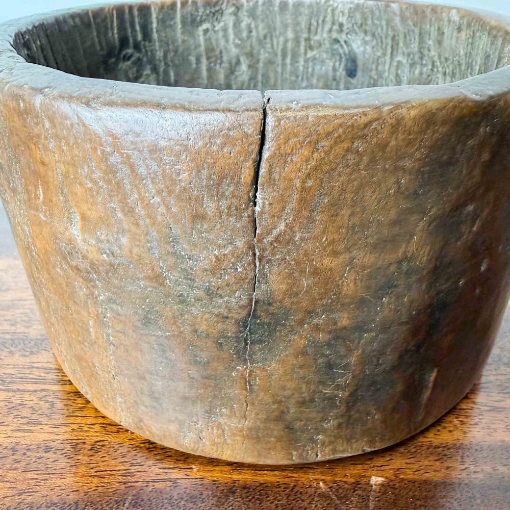 A round hand-carved antique wooden bowl with thick walls and a patinated brown timber surface. View X