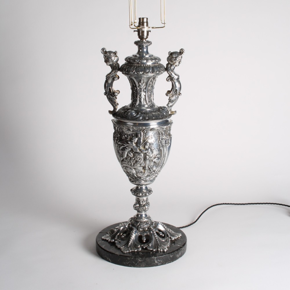 A polished silver-toned spelter table lamp base in the shape of a classical urn with relief carvings and creature handles on a circular marble plinth. View III