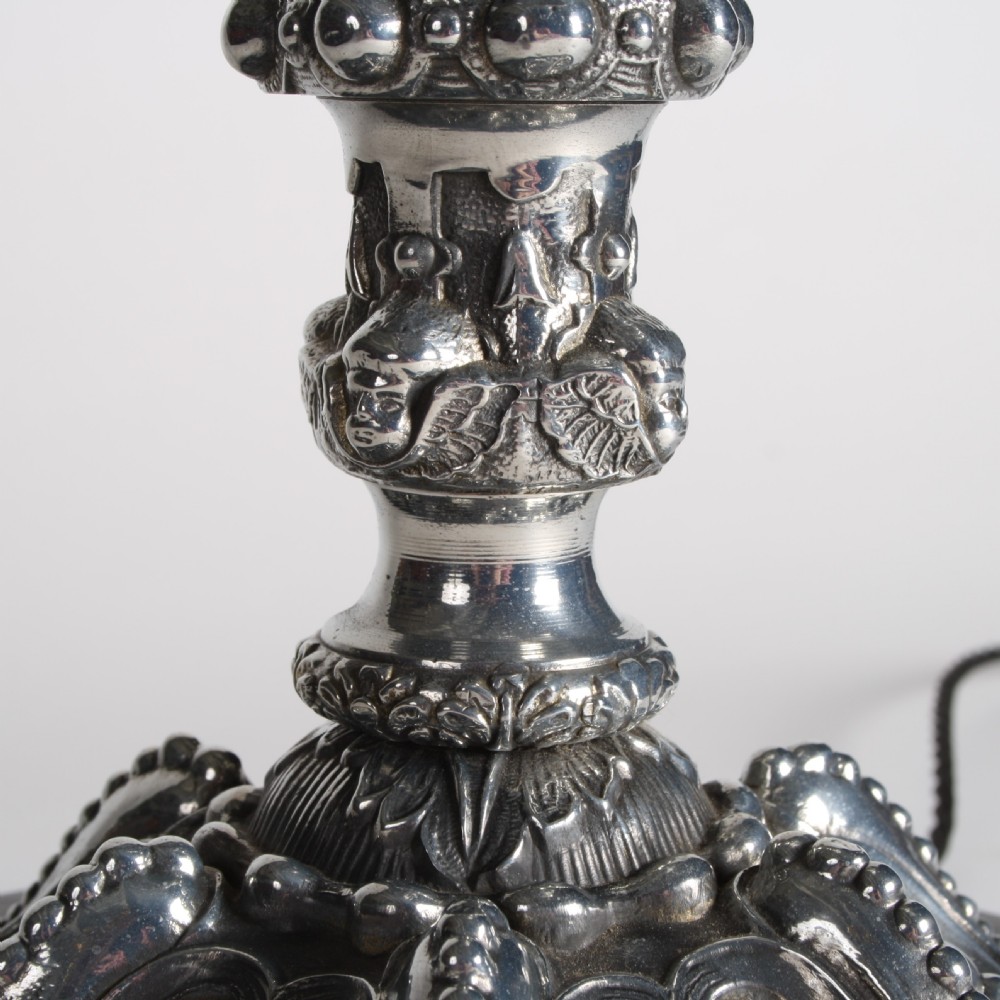 A polished silver-toned spelter table lamp base in the shape of a classical urn with relief carvings and creature handles on a circular marble plinth. View V