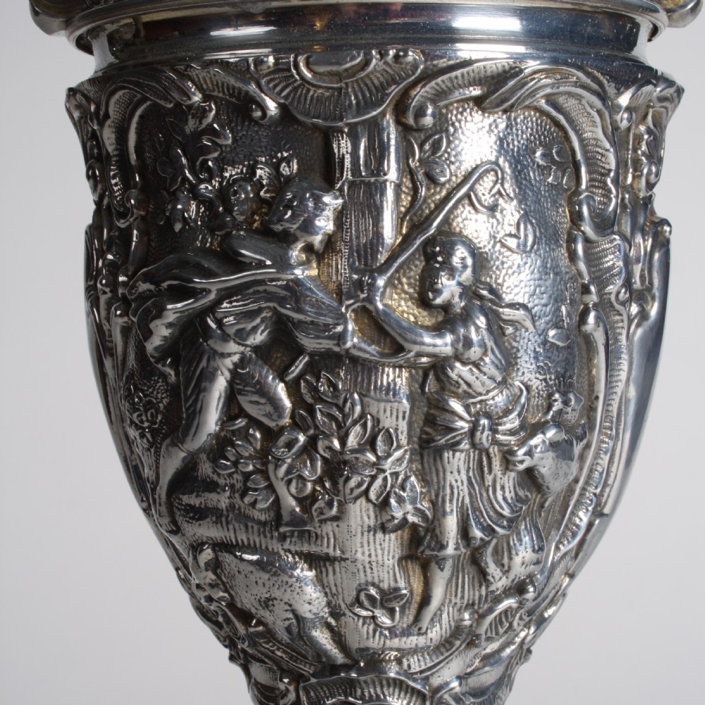 A polished silver-toned spelter table lamp base in the shape of a classical urn with relief carvings and creature handles on a circular marble plinth. View VI