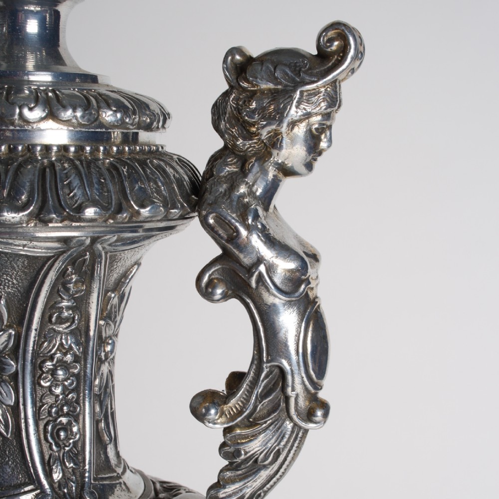 A polished silver-toned spelter table lamp base in the shape of a classical urn with relief carvings and creature handles on a circular marble plinth. View VII