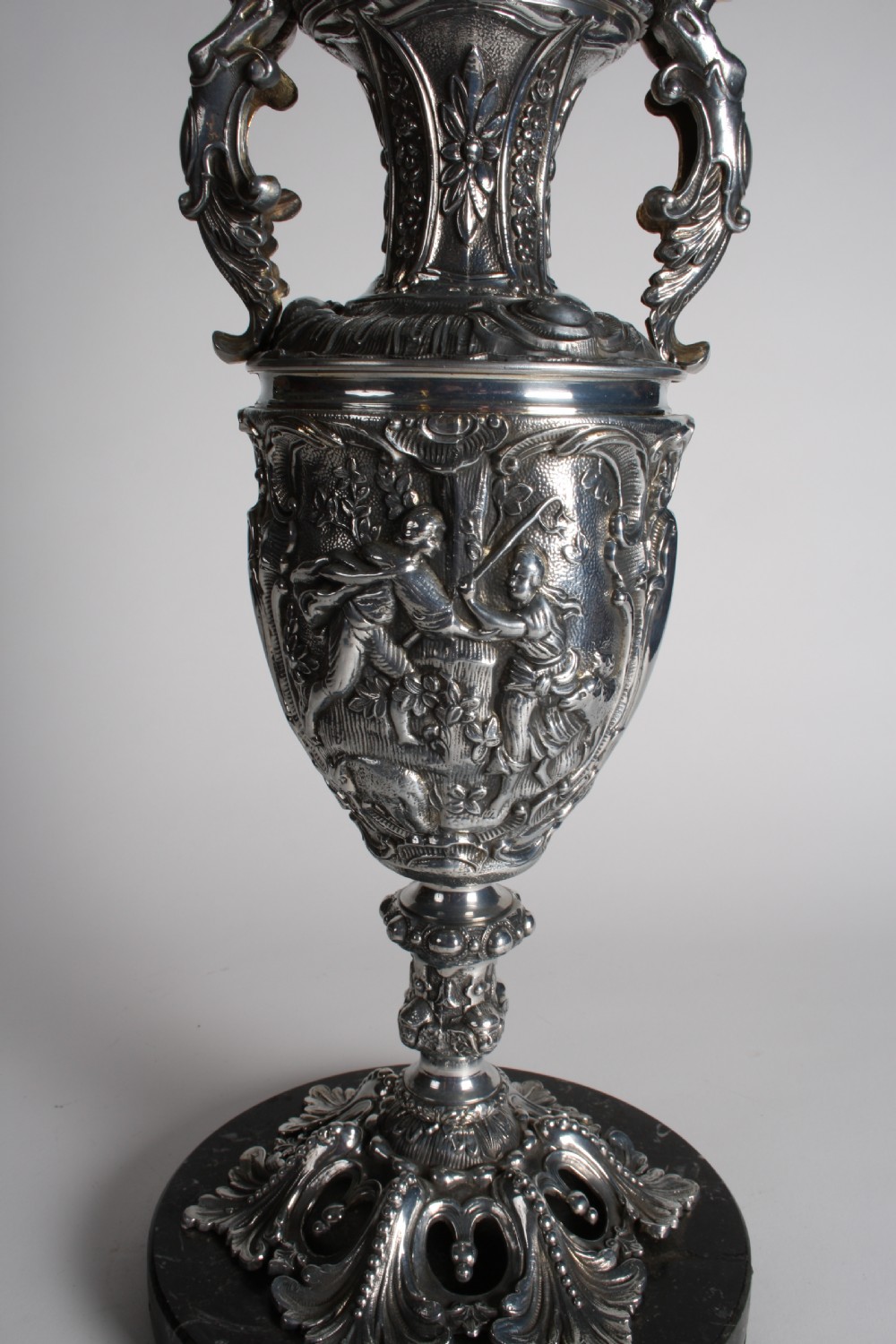 A polished silver-toned spelter table lamp base in the shape of a classical urn with relief carvings and creature handles on a circular marble plinth. View XI