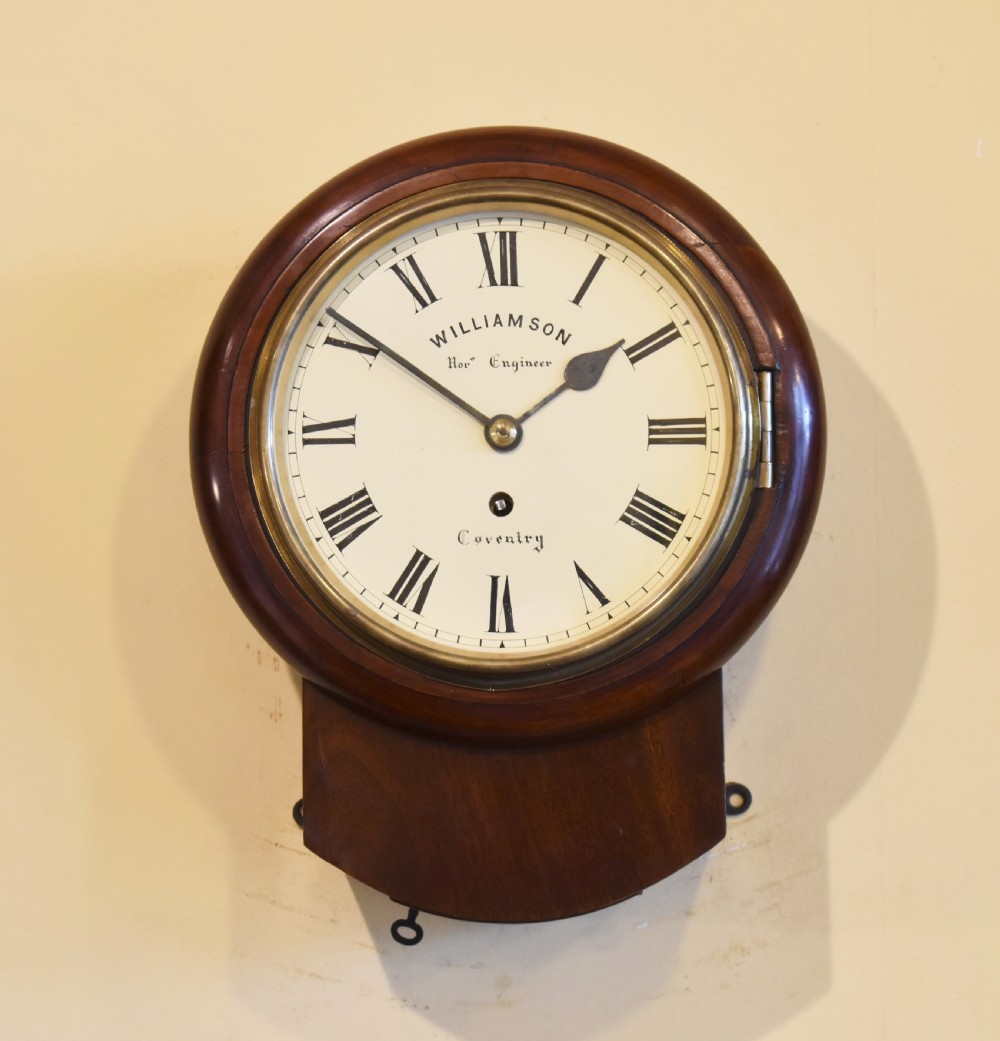 An antique mahogany wall clock featuring a white circular dial with Roman numerals enclosed in a brass bezel above a curved wood drop case.