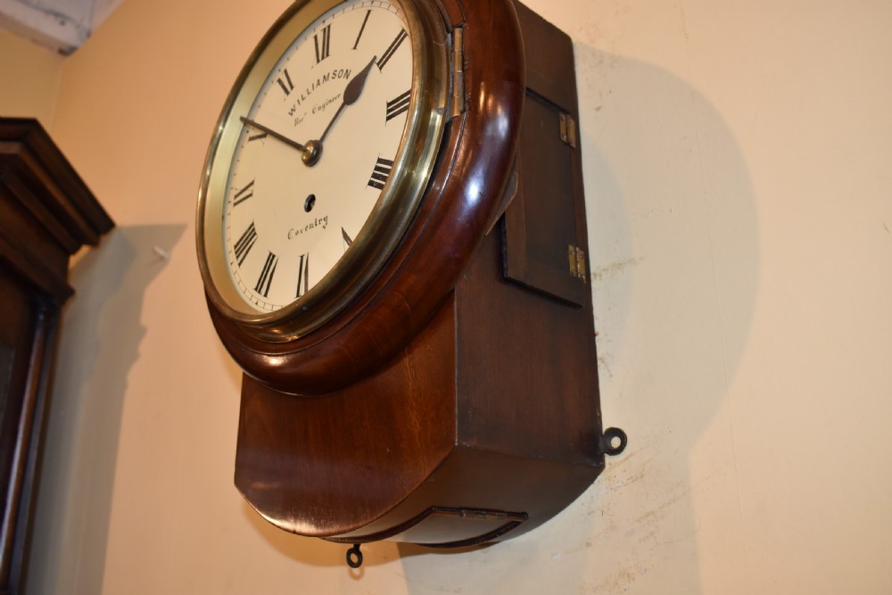 An antique mahogany wall clock featuring a white circular dial with Roman numerals enclosed in a brass bezel above a curved wood drop case. View II