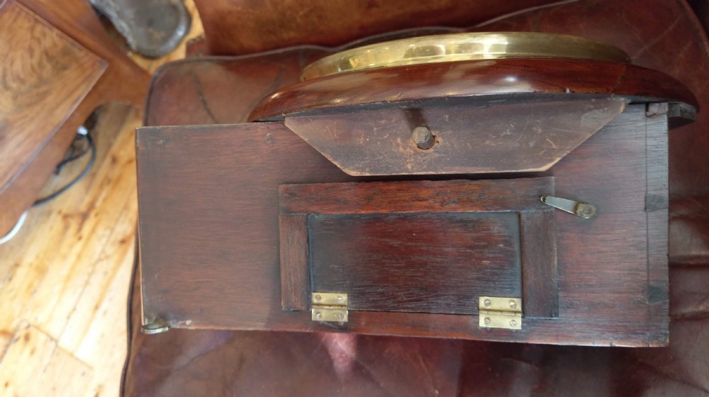 An antique mahogany wall clock featuring a white circular dial with Roman numerals enclosed in a brass bezel above a curved wood drop case. View IX