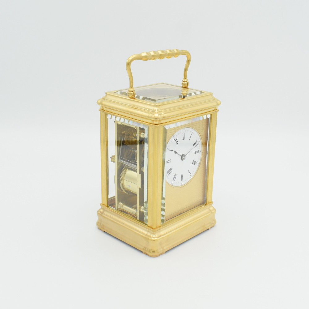 A nineteenth-century French gilt brass carriage clock featuring a rectangular case with glass panels, a top carrying handle, and a white enamel dial with Roman numerals. View VI