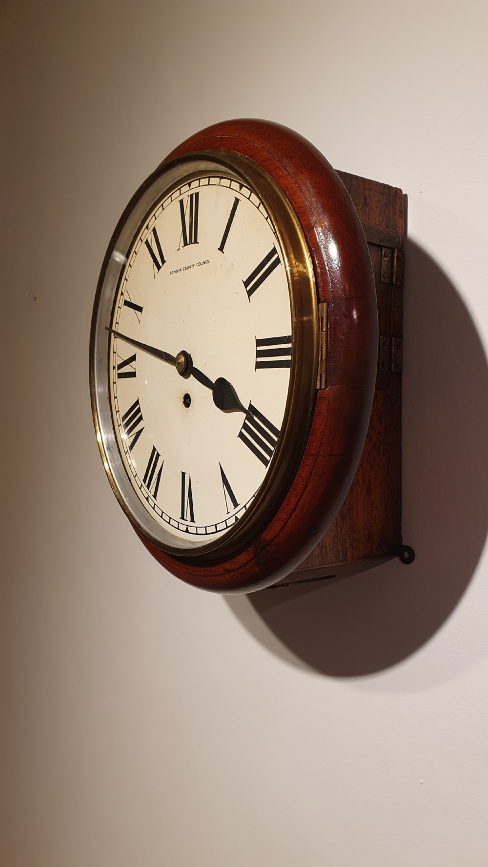 A circular antique mahogany wall clock featuring an off-white dial with black Roman numerals, black hands, and London County Council text. View IV