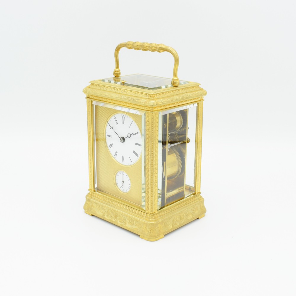 An antique gilded brass carriage clock featuring an engraved case, white enamel dial with Roman numerals, and bevelled glass panels. View II