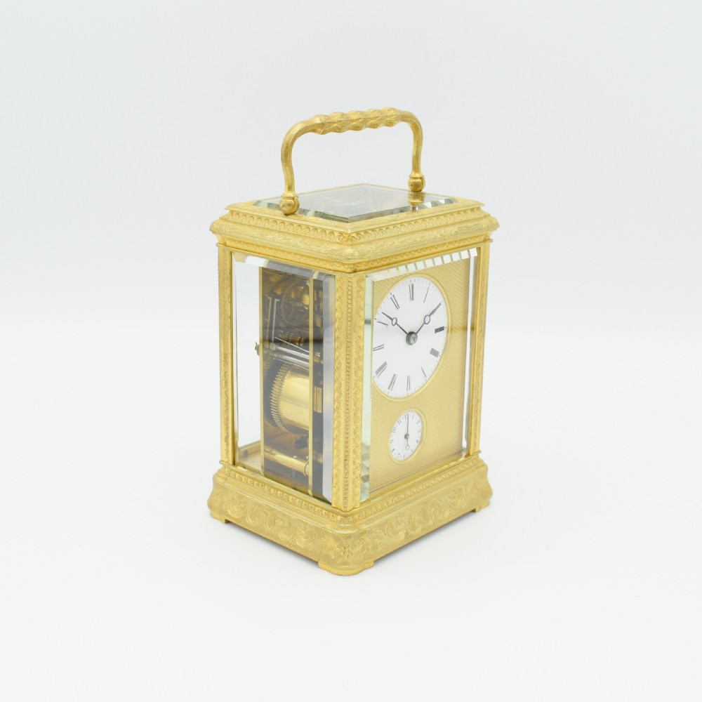 An antique gilded brass carriage clock featuring an engraved case, white enamel dial with Roman numerals, and bevelled glass panels. View III