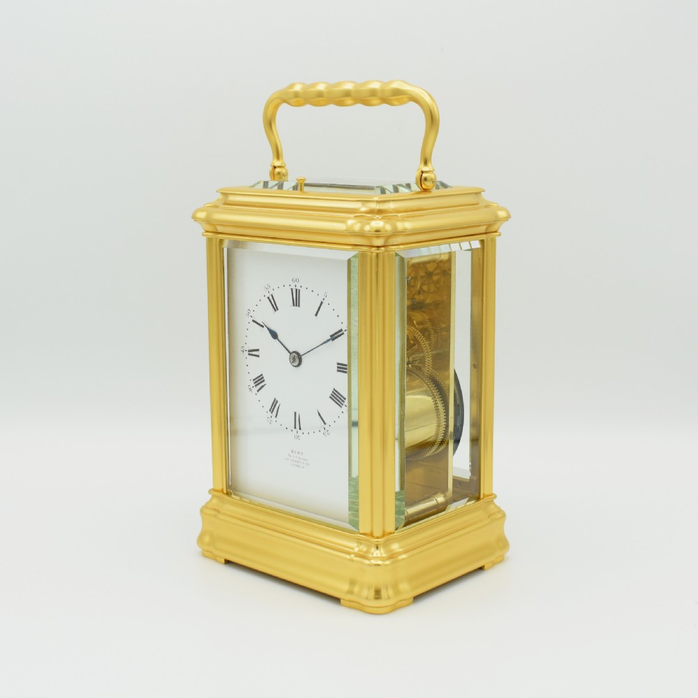 A gilded brass carriage clock featuring a shaped top carrying handle, clear bevelled glass panels, and a white enamel dial with Roman numerals. View II