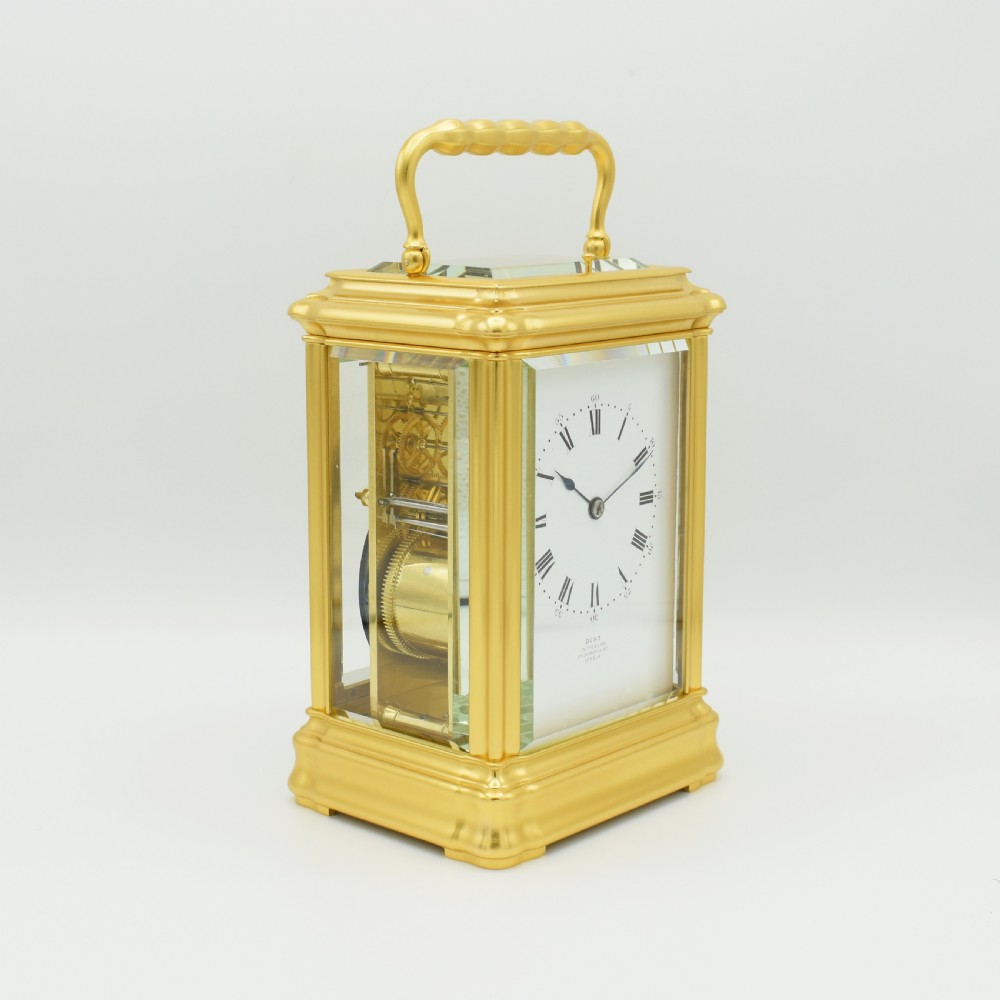 A gilded brass carriage clock featuring a shaped top carrying handle, clear bevelled glass panels, and a white enamel dial with Roman numerals. View III