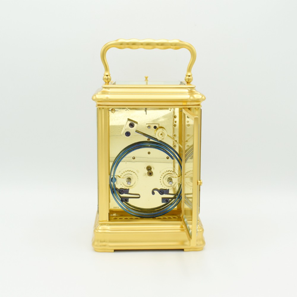 A gilded brass carriage clock featuring a shaped top carrying handle, clear bevelled glass panels, and a white enamel dial with Roman numerals. View V