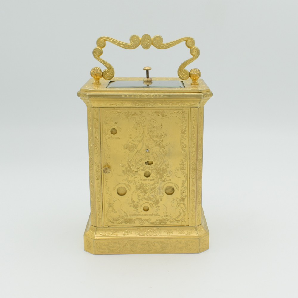 An antique gilded brass carriage clock with an ornate handle, detailed chasing on the case, and a white enamel dial. View III