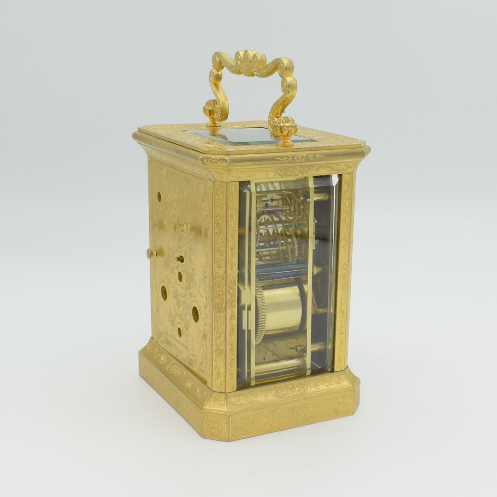 An antique gilded brass carriage clock with an ornate handle, detailed chasing on the case, and a white enamel dial. View IV