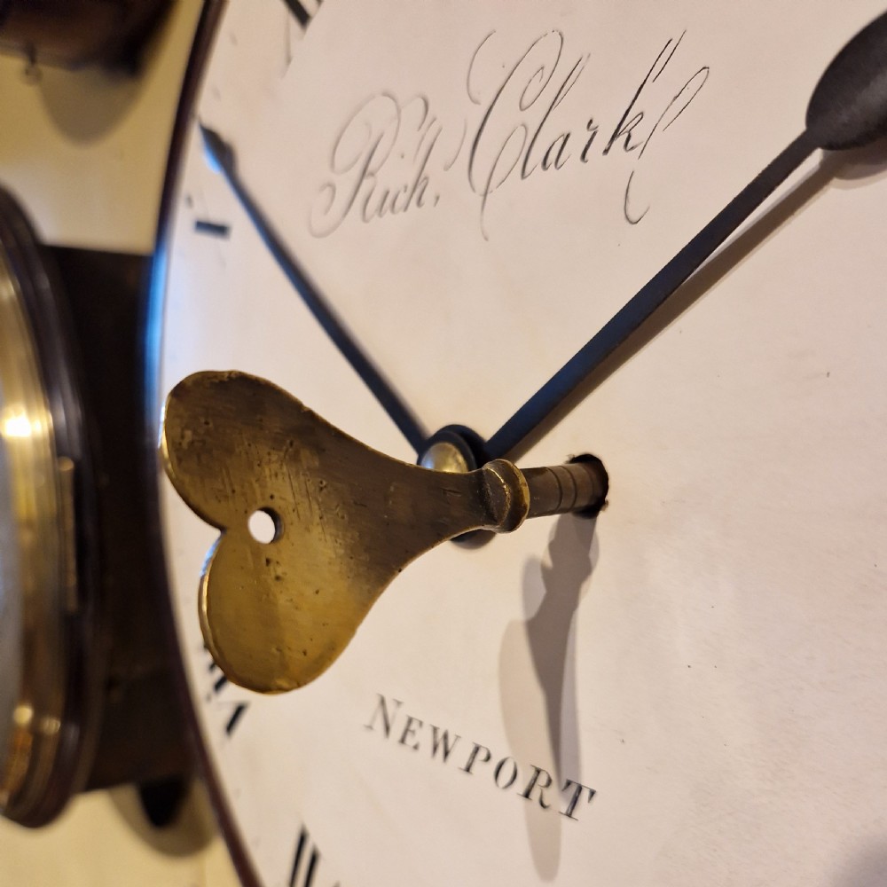 An antique circular fusee wall clock featuring a dark mahogany surround, brass bezel, and a white dial with Roman numerals signed Richd Clark Newport. View VIII