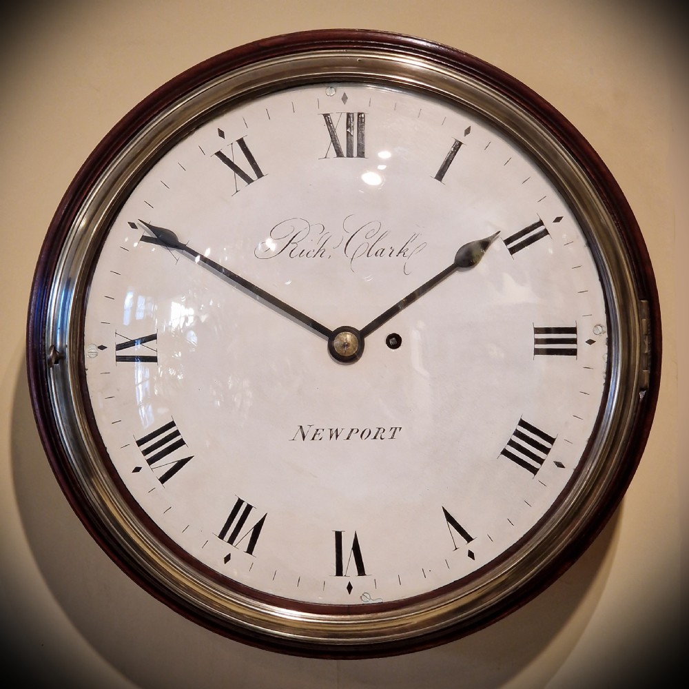 An antique circular fusee wall clock featuring a dark mahogany surround, brass bezel, and a white dial with Roman numerals signed Richd Clark Newport. View IX