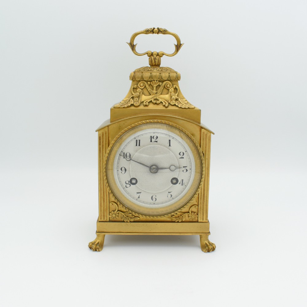 A French gilt bronze officer clock featuring a top loop handle, chased relief ornament, white circular dial with Arabic numerals, and four paw feet.