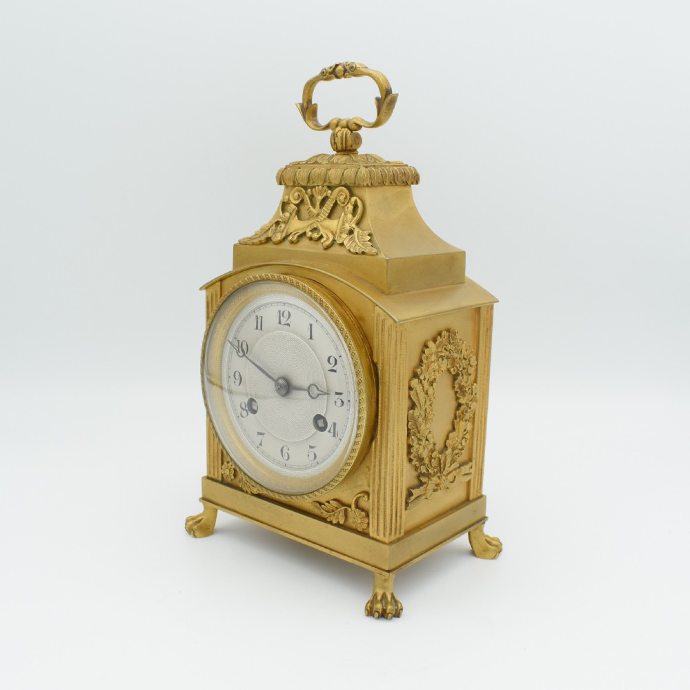 A French gilt bronze officer clock featuring a top loop handle, chased relief ornament, white circular dial with Arabic numerals, and four paw feet. View II