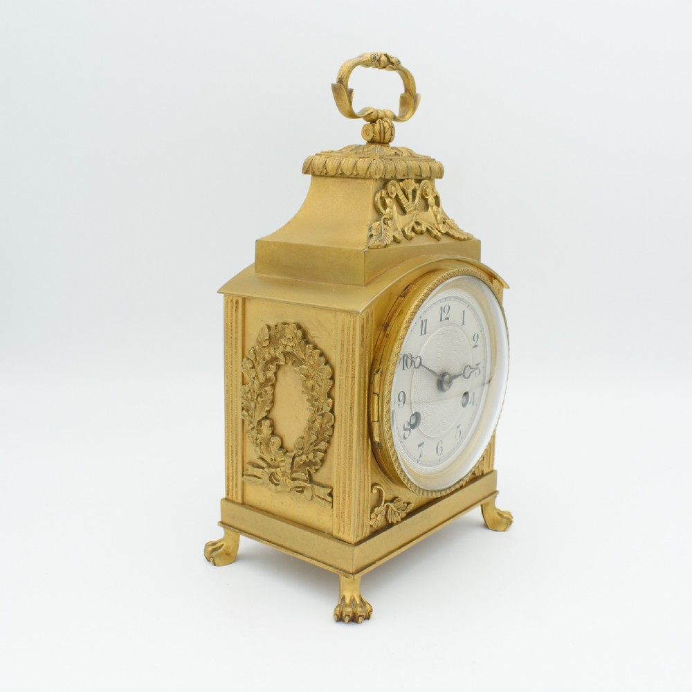 A French gilt bronze officer clock featuring a top loop handle, chased relief ornament, white circular dial with Arabic numerals, and four paw feet. View III