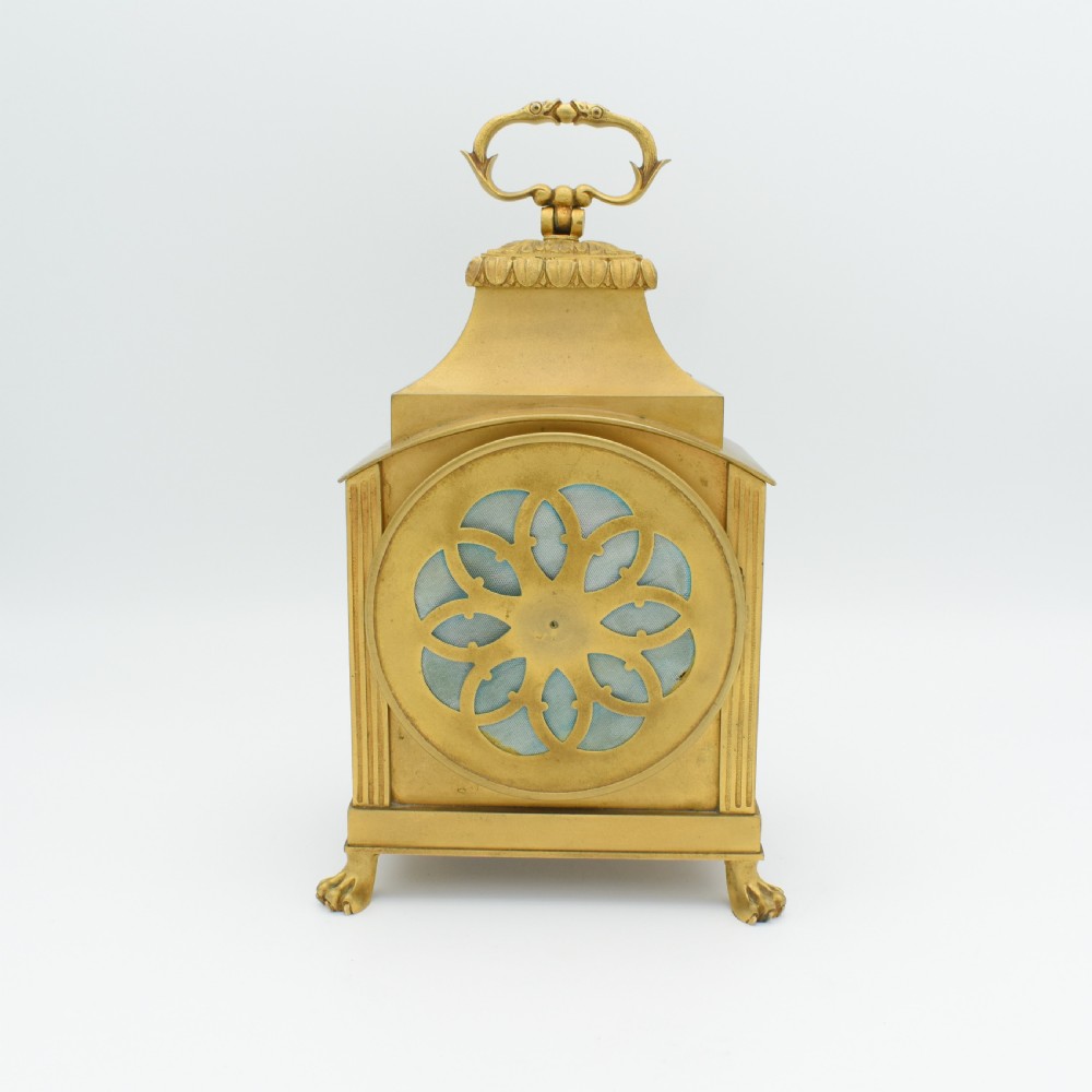 A French gilt bronze officer clock featuring a top loop handle, chased relief ornament, white circular dial with Arabic numerals, and four paw feet. View V