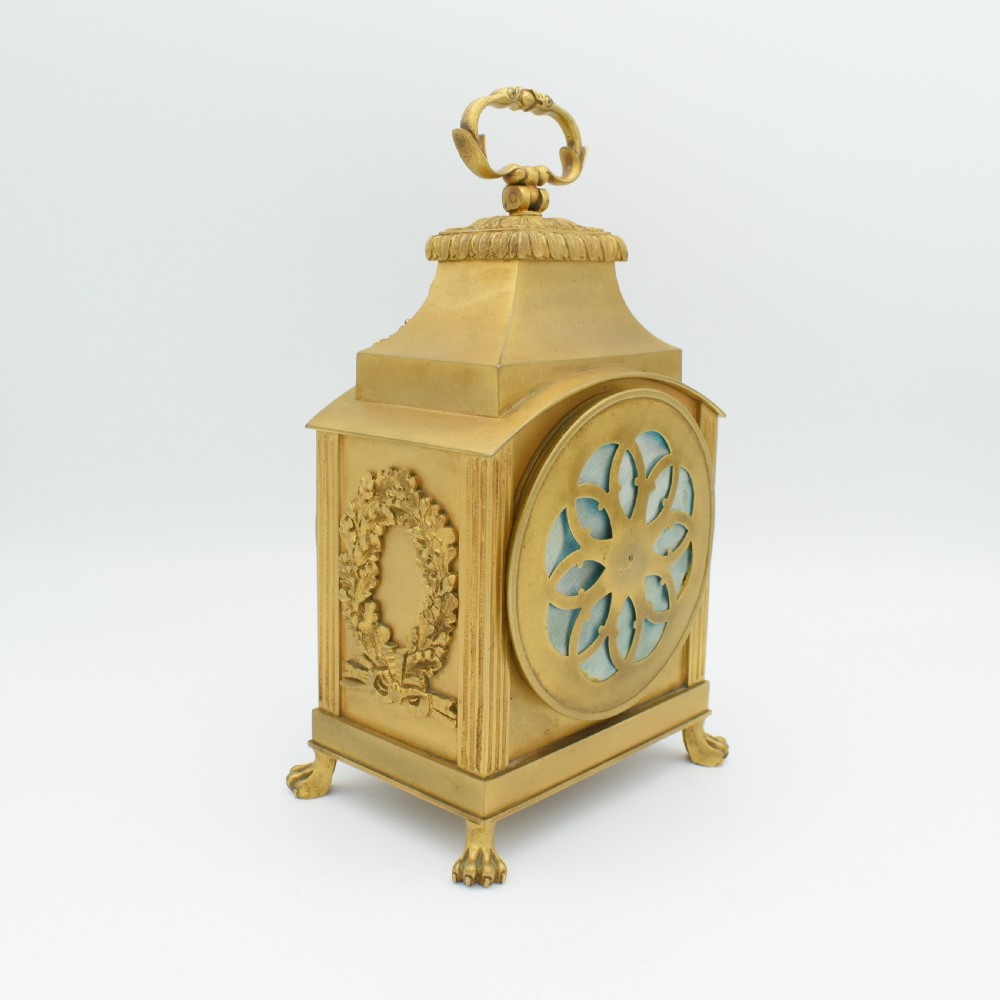 A French gilt bronze officer clock featuring a top loop handle, chased relief ornament, white circular dial with Arabic numerals, and four paw feet. View VI