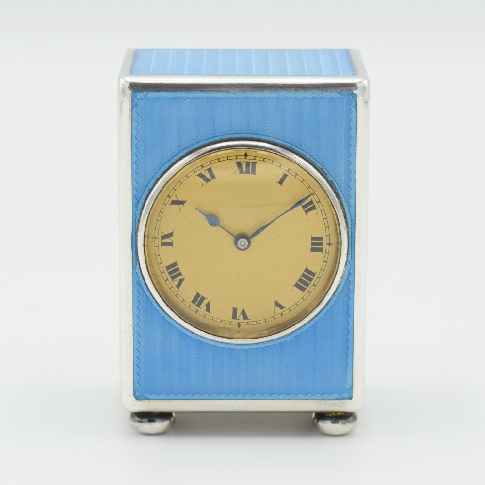 An Art Deco rectangular miniature clock featuring sky blue guilloche enamel casing with a circular dial, Roman numerals, and silver ball feet. View II