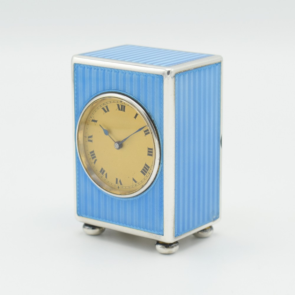 An Art Deco rectangular miniature clock featuring sky blue guilloche enamel casing with a circular dial, Roman numerals, and silver ball feet. View III