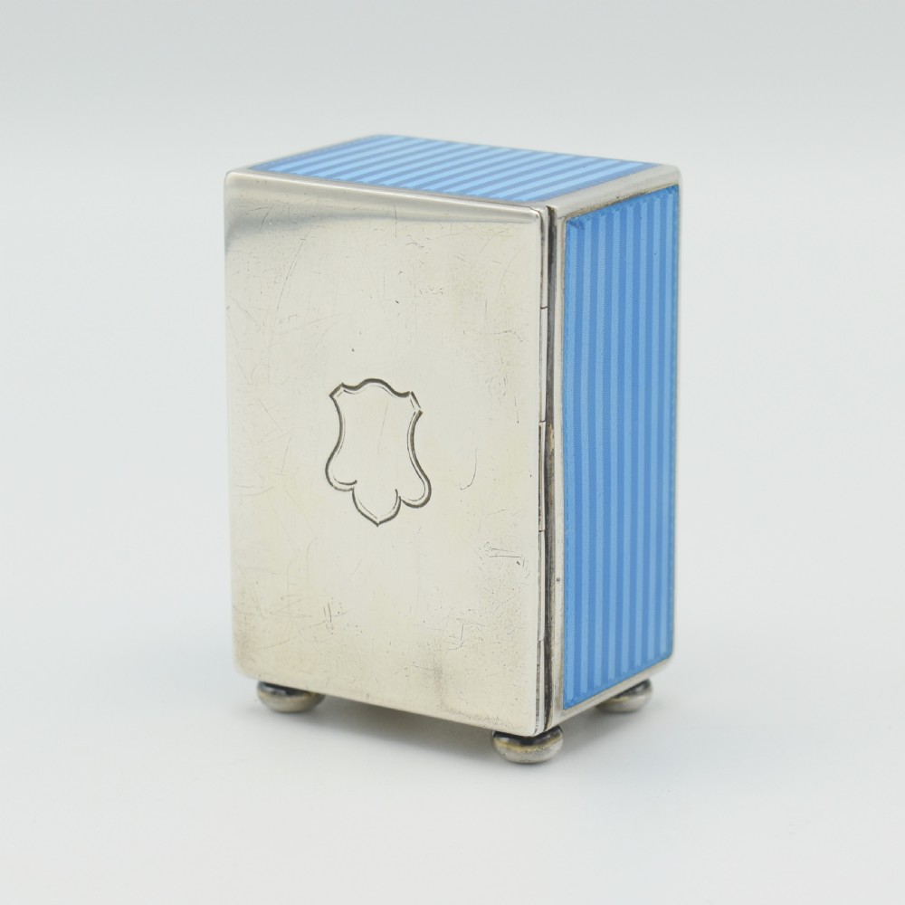 An Art Deco rectangular miniature clock featuring sky blue guilloche enamel casing with a circular dial, Roman numerals, and silver ball feet. View V