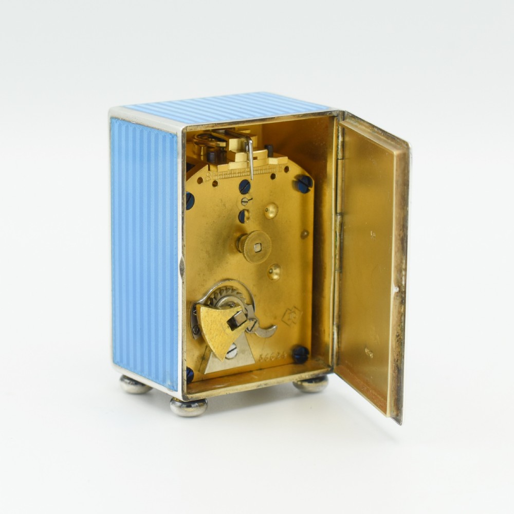 An Art Deco rectangular miniature clock featuring sky blue guilloche enamel casing with a circular dial, Roman numerals, and silver ball feet. View VI