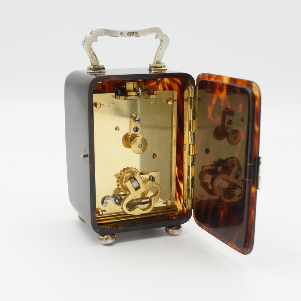 An Edwardian rectangular tortoiseshell timepiece featuring silver bun feet, a silver carrying handle, and a white enamel clock dial with Roman numerals. View III
