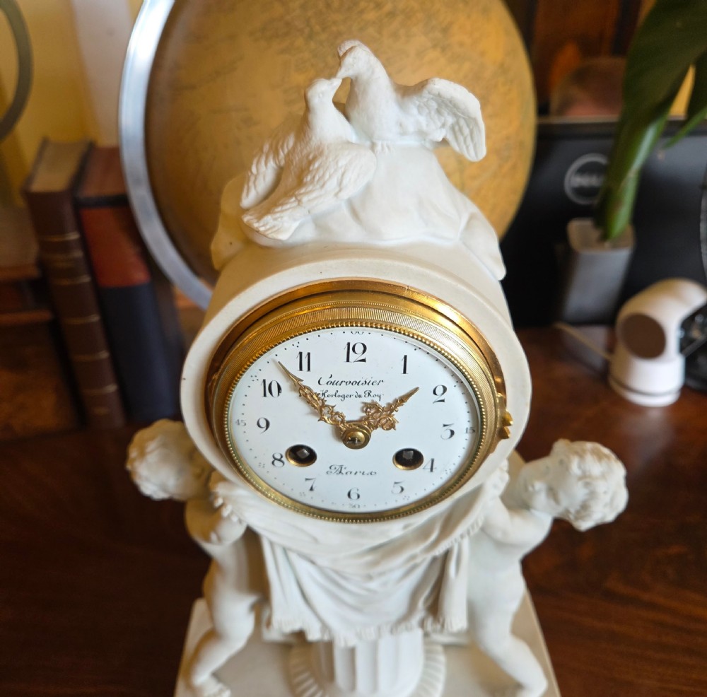 A white bisque porcelain Neoclassical mantel clock featuring two putti flanking a fluted column topped with a pair of doves. View III