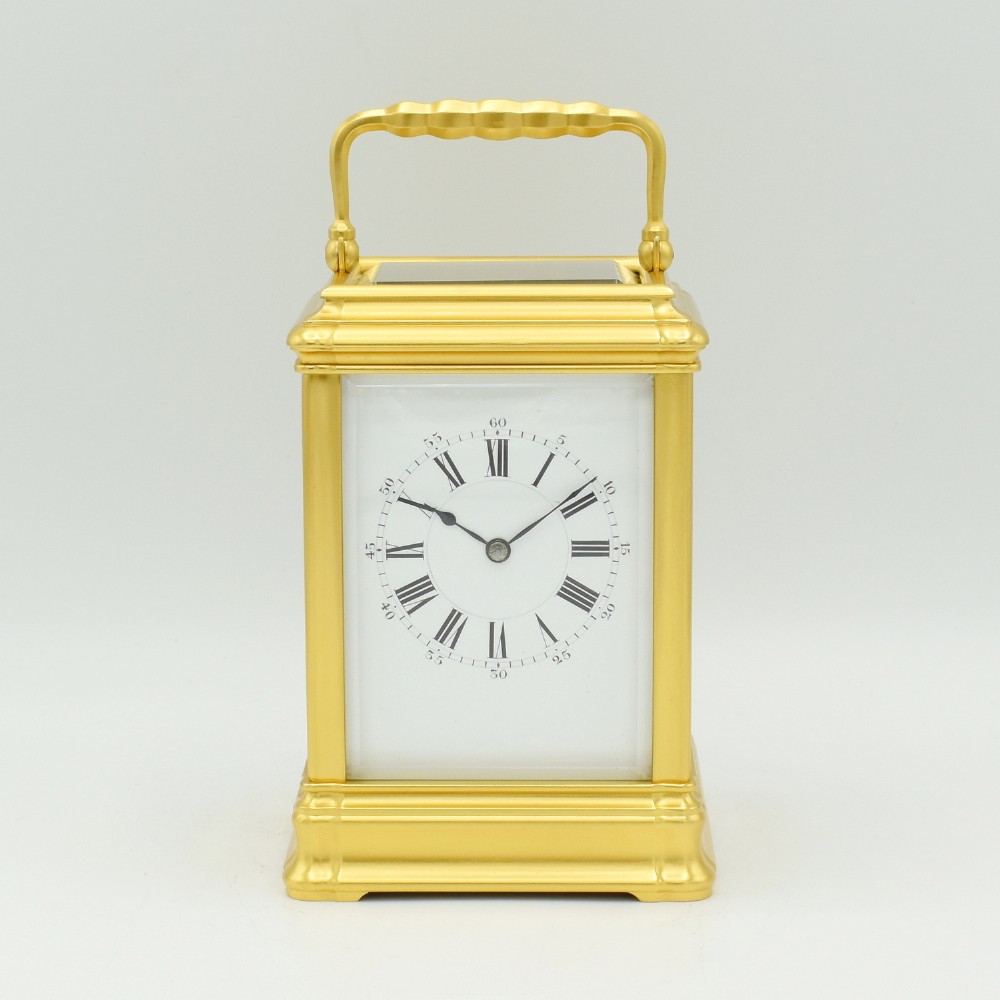 An antique French carriage clock featuring a rectangular gilt brass corniche case with glass panels, an articulated carrying handle, and a white enamel dial with Roman numerals.